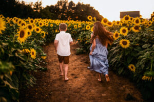 boy and girl running through the field away from the camera through sunflowers